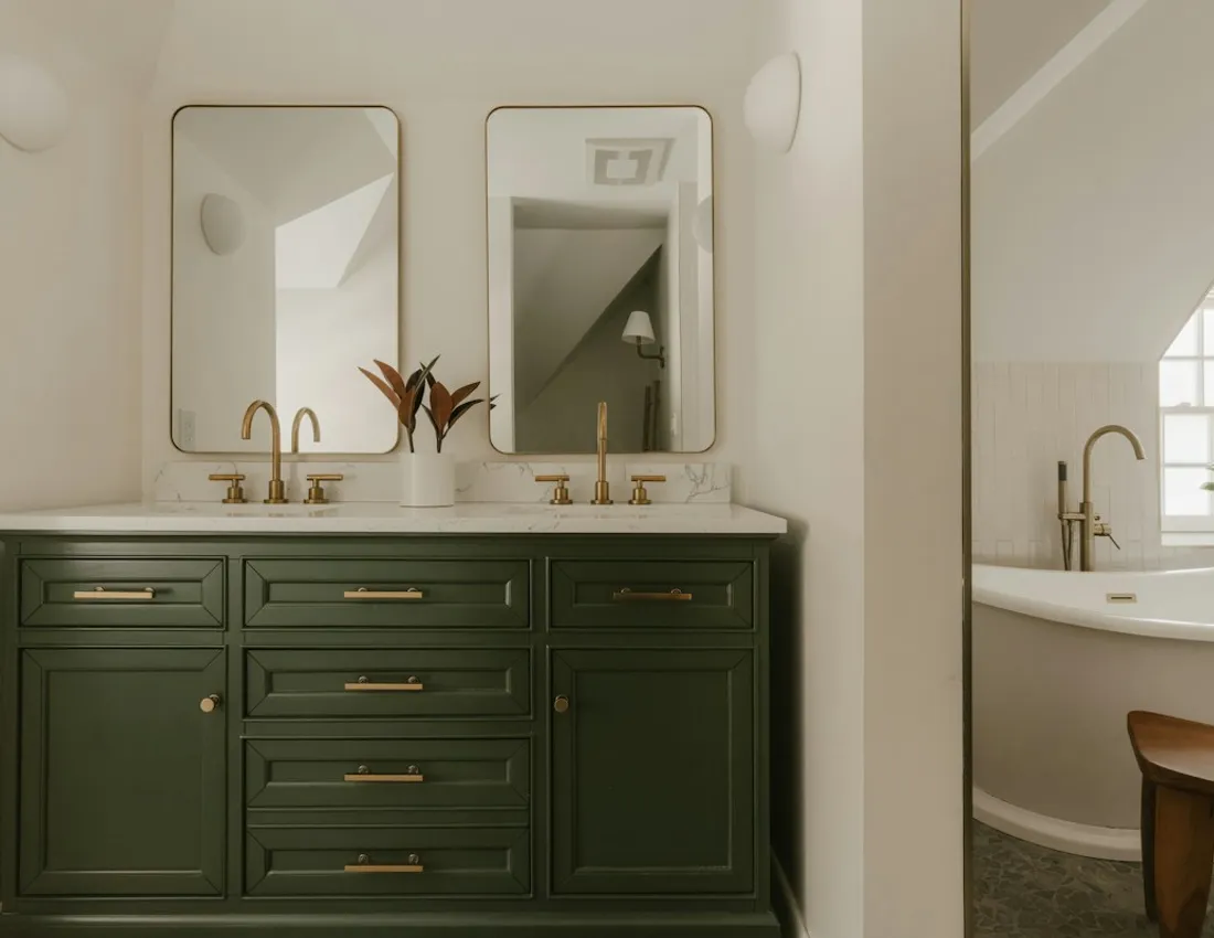 A green bathroom vanity with brass handles and twin mirrors