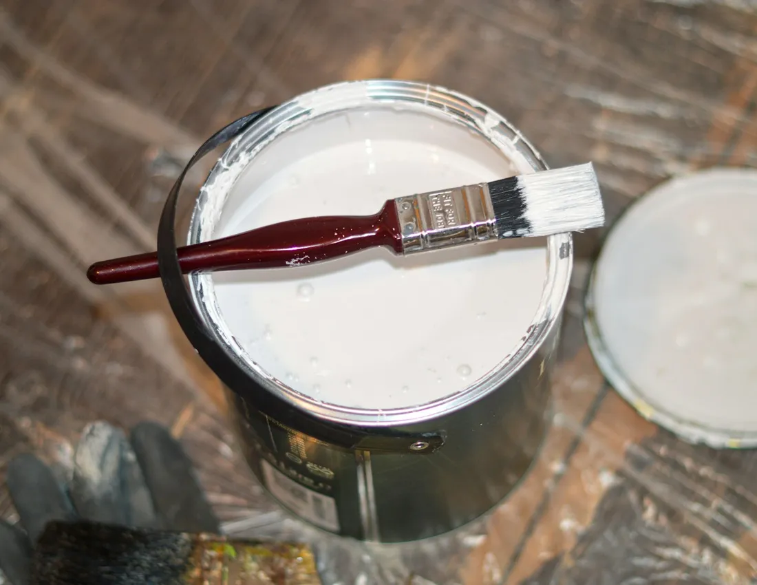 A brush resting across an open tin of white paint